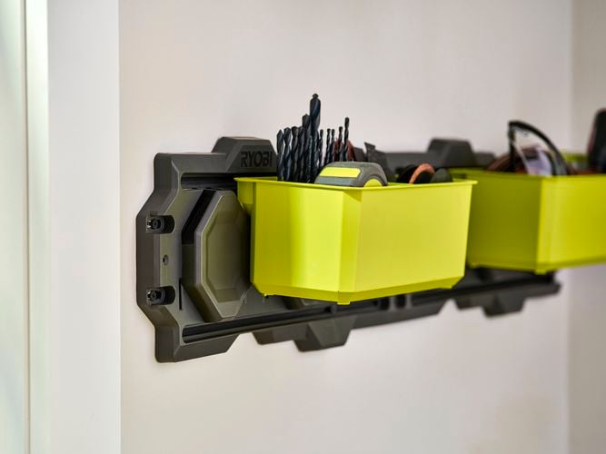 Green tub hanging on a wall rail with small items inside.