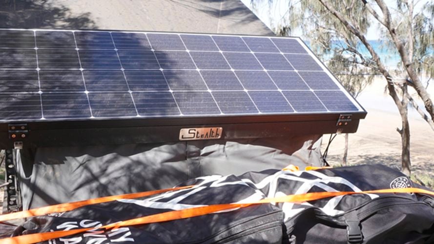 KT solar panel mounted on a camper trailer beside a beach during an outdoor camping trip.
