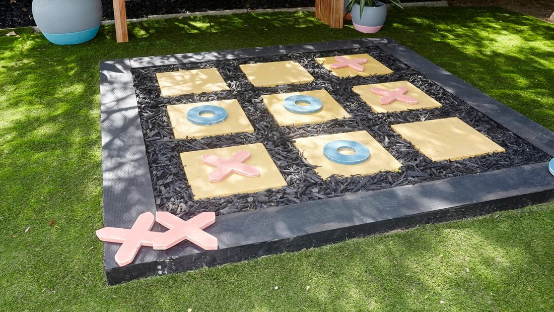 An outside noughts and crosses game made with pavers on a bed of sand with a border of sleepers