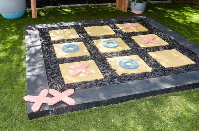 An outside noughts and crosses game made with pavers on a bed of sand with a border of sleepers