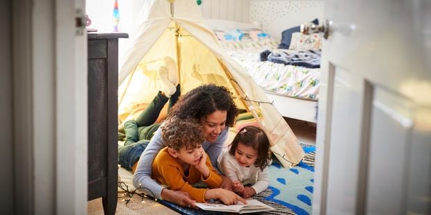 Mother and 2 children reading a book in a play tent.