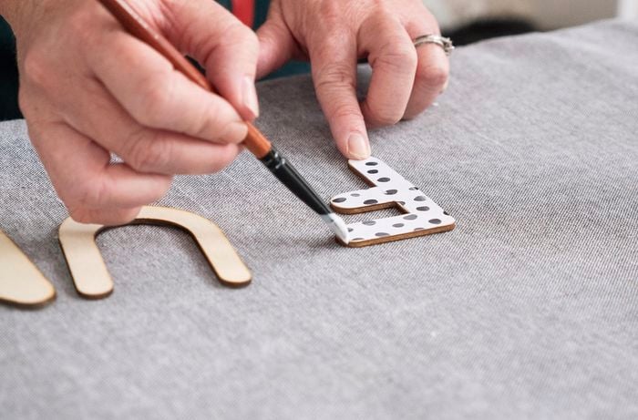 Person applying glue to wooden letter.