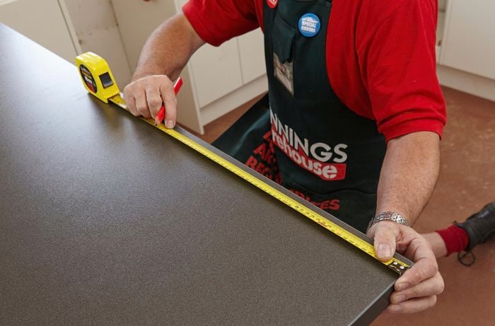 A person measuring a laminated benchtop