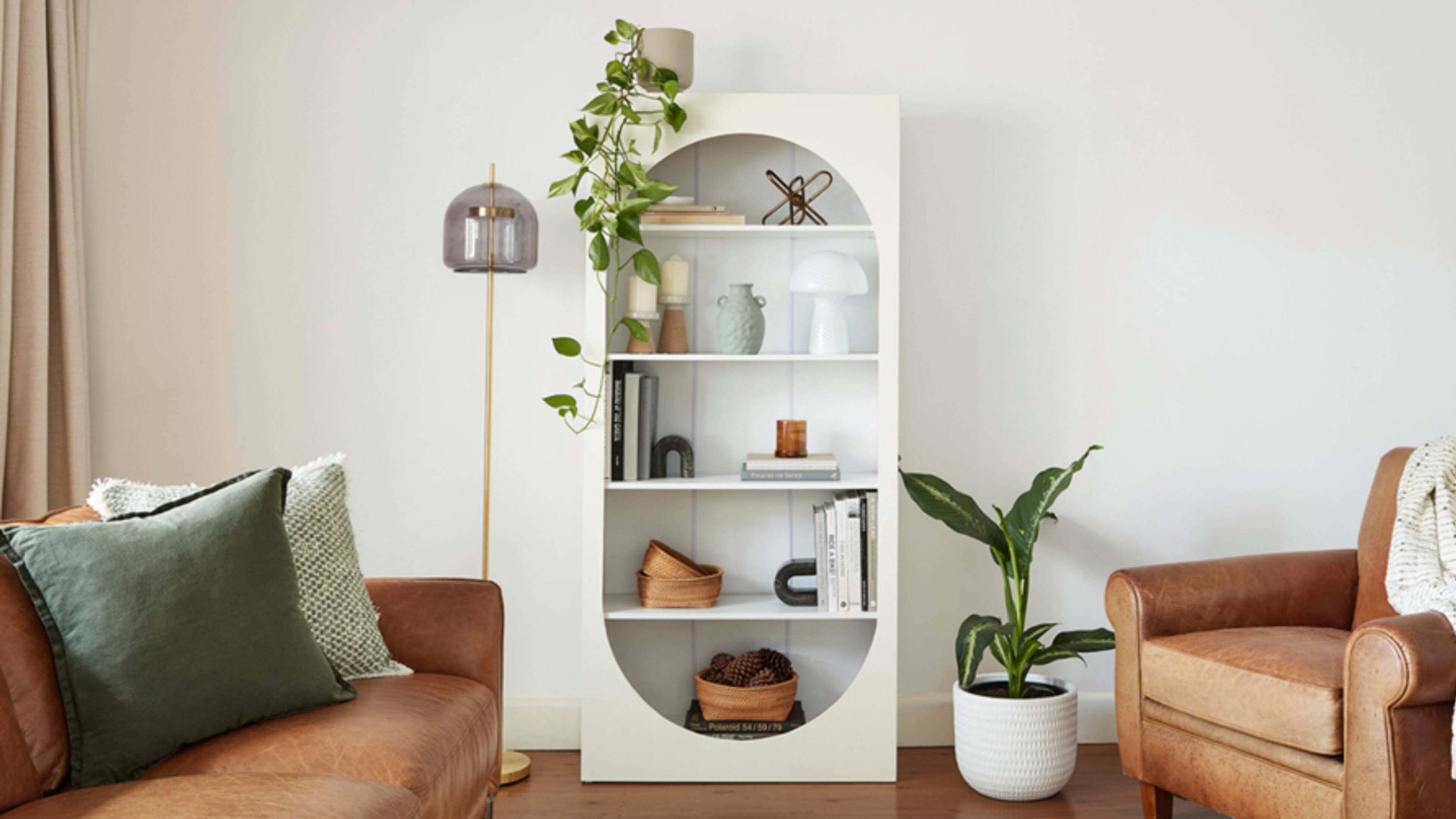 White modern book shelf in a room with pot plants and a couch