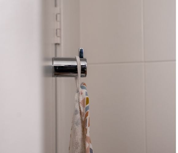 Minimalist chrome hook in cylindrical shape hangs off back of bathroom door