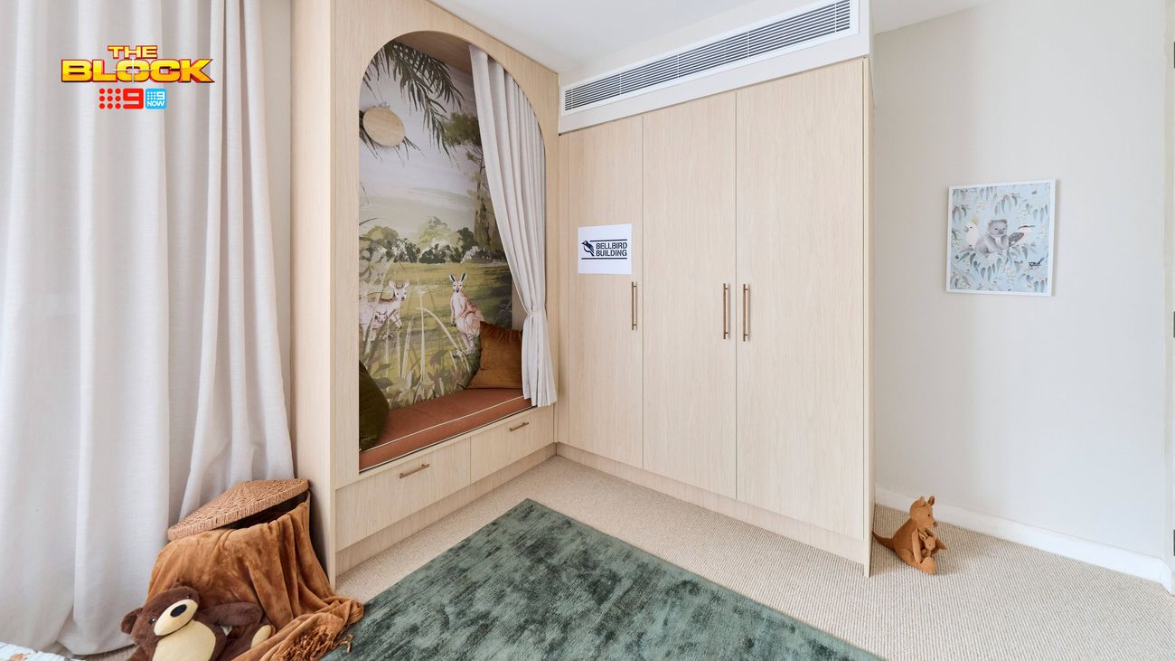 Children’s bedroom featuring built-in timber wardrobes, a window seat with a nature mural, floor-to-ceiling curtains and a soft green rug.