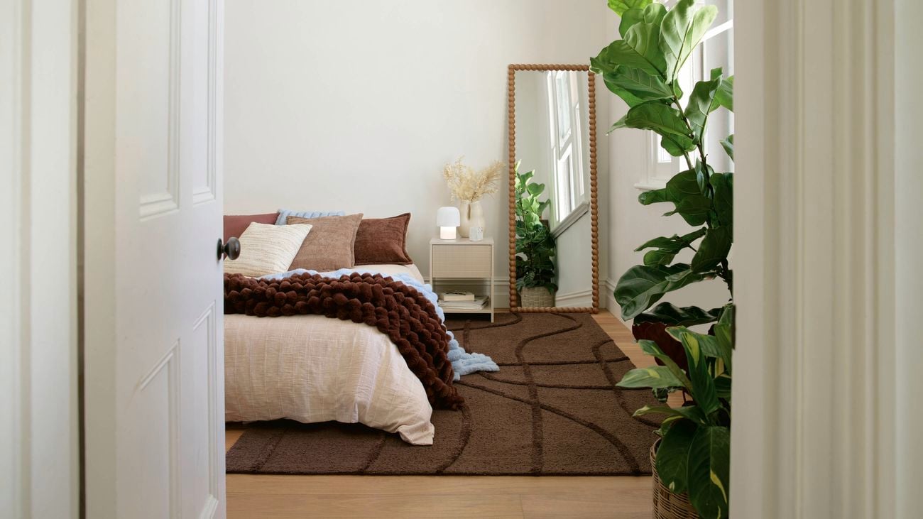 Bedroom styled with a large rug under the bed, layered bedding, floor mirror and indoor plants.