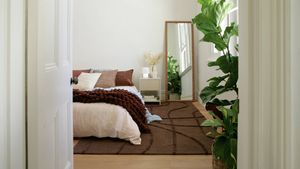 Bedroom styled with a large rug under the bed, layered bedding, floor mirror and indoor plants.