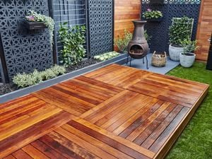 A welcoming wooden patio space with outside fire, wood, BBQ and potted plants.