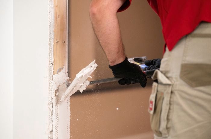 A person wearing gloves is using a pry bar to remove any existing plaster and external angles around the arch.