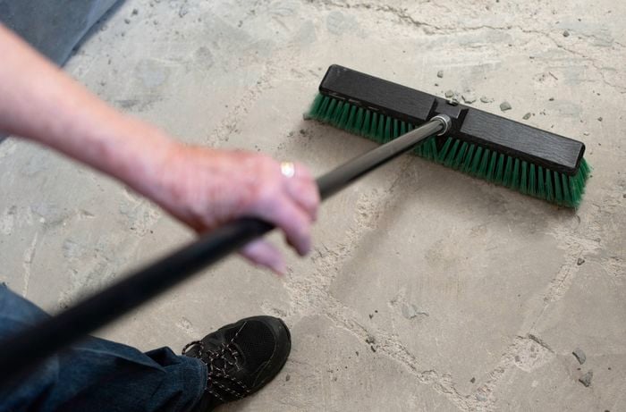 A person is sweeping remaining debris from a concrete floor with a broom after removing tiles