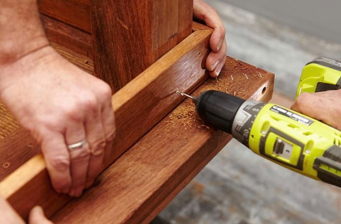 Person drilling timber table top and leg together.