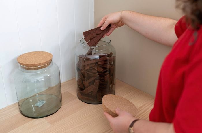 A Bunnings Team Member is placing dog treats into a clear large glass jar container with a cork lid.