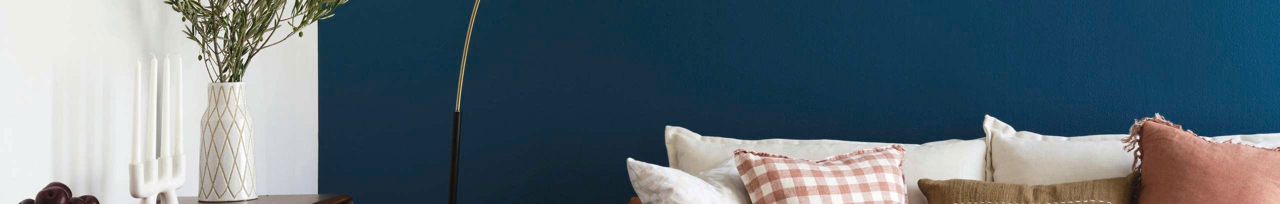 Living room with blue feature wall, brass arc floor lamp and white sofa with coloured cushions.