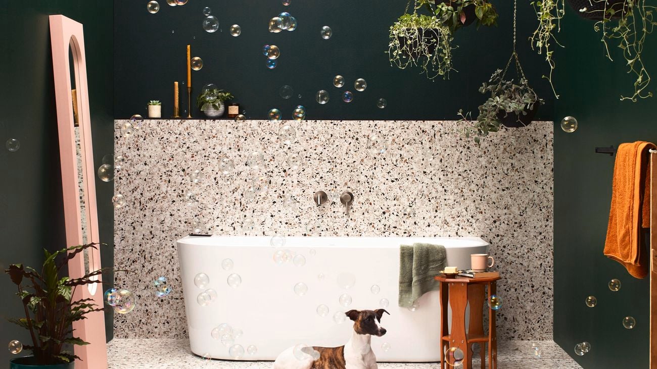 A bathroom with a bath, dog, pot plants and a table next to bath.