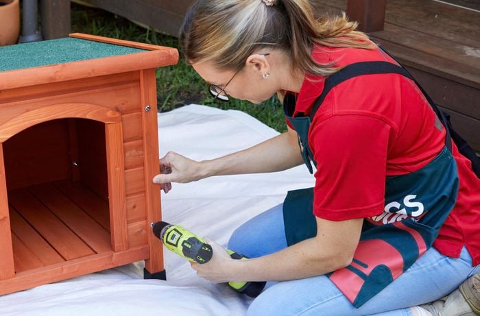A woman assembles a dog kennel on a drop sheet