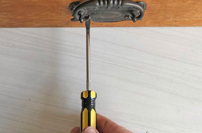 Person using a screwdriver to remove handle from a wooden drawer