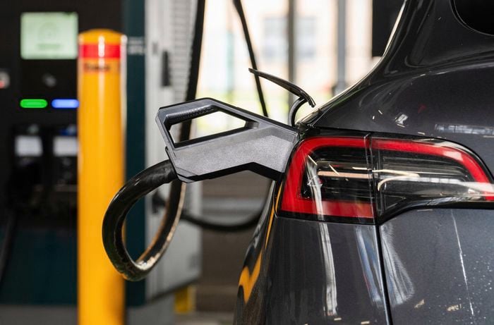 A close-up view of an electric vehicle charging connector plugged into the rear of a Tesla at a fast-charging station.