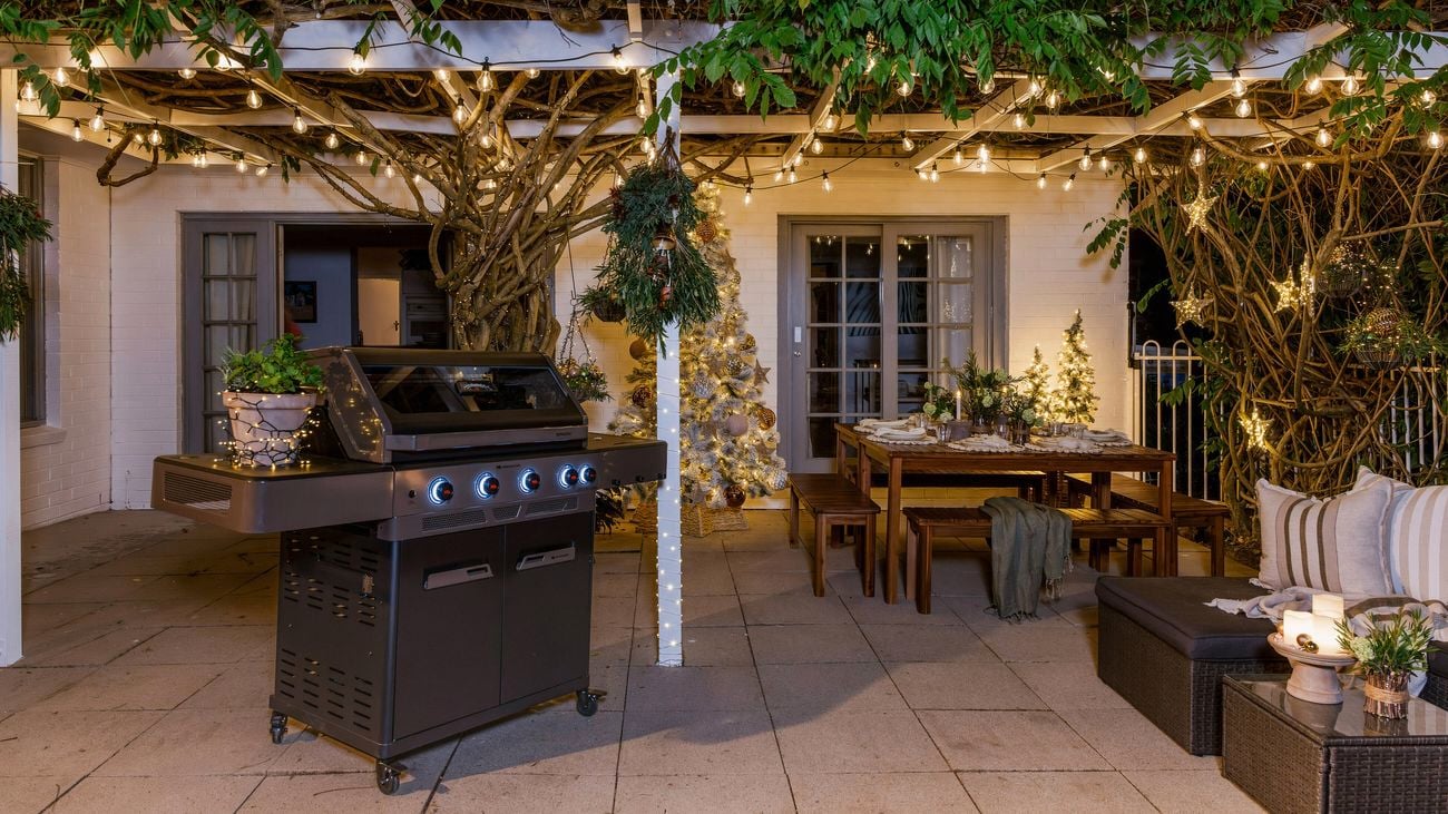 Outdoor entertaining area with a barbecue, decorated dining table, and Christmas lights.