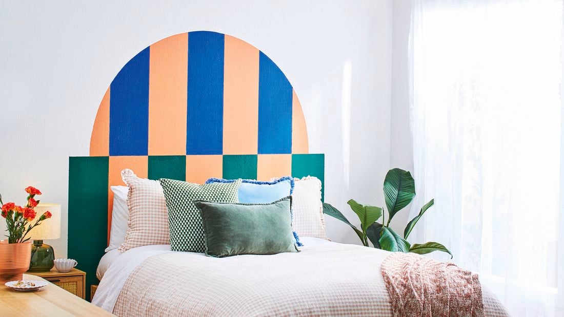 A D.I.Y. bed headboard in green, blue and apricot behind a double bed piled with pillows