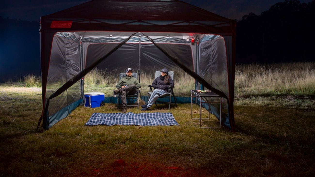 Two people sitting on camping chairs in a lit gazebo at night