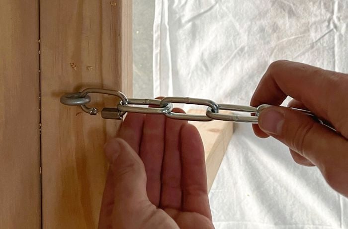Hands attaching a metal chain to an eye bolt in a timber surface.