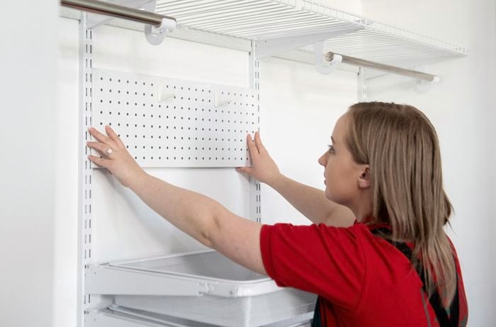 A person installing a pegboard at the back of a wardrobe