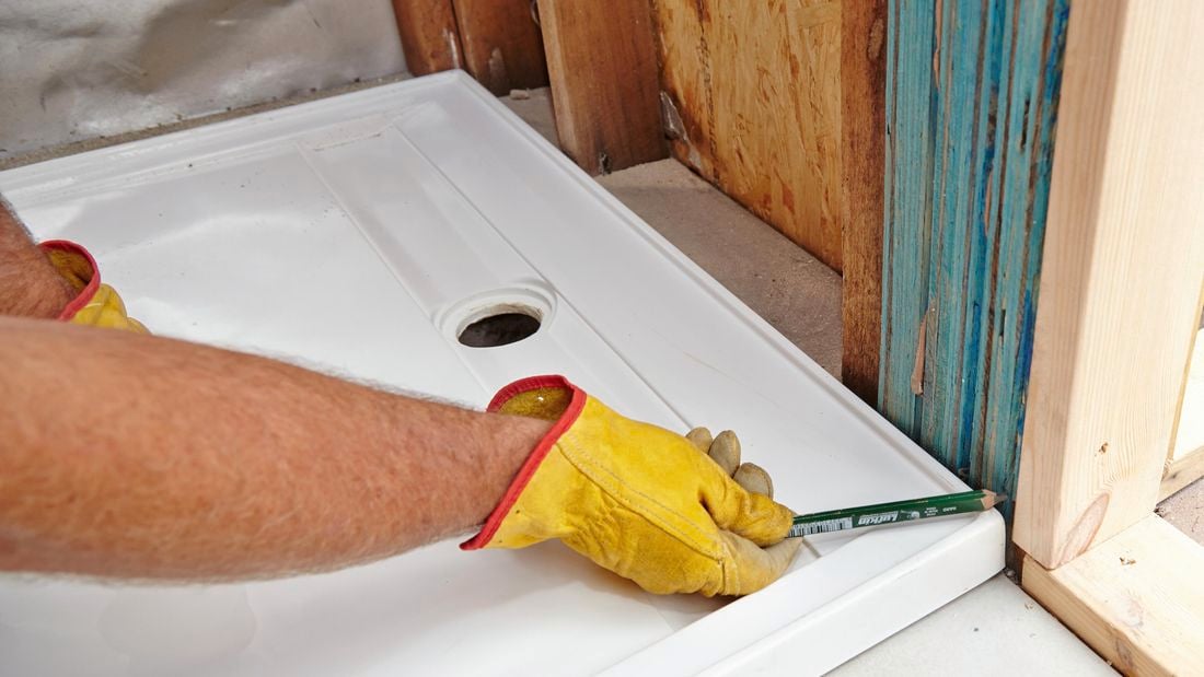 A pencil being used to mark cutting lines on a wall frame to make room for a shower base
