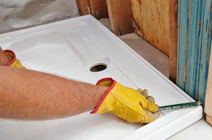 A pencil being used to mark cutting lines on a wall frame to make room for a shower base