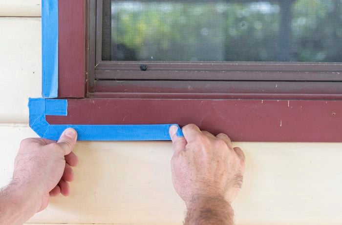 A person masking around a window with masking tape
