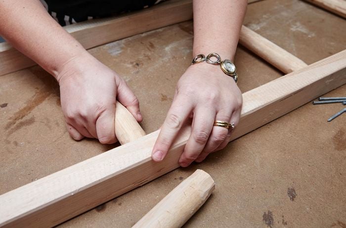 Person insert ladder rung in between two pieces of timber.