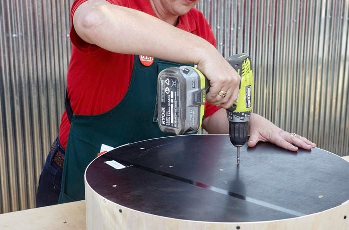 A person screwing through the back of a circle of plywood using a cordless drill
