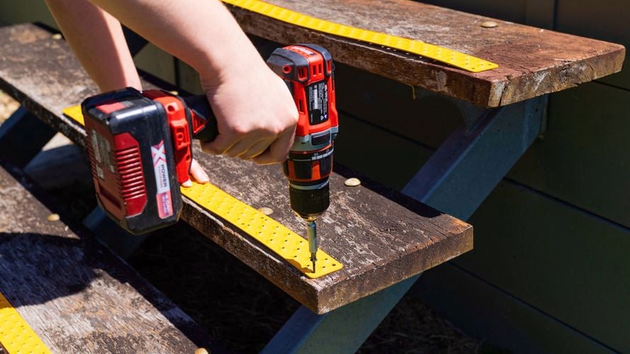 Person attaching a tread to stairs with drill.