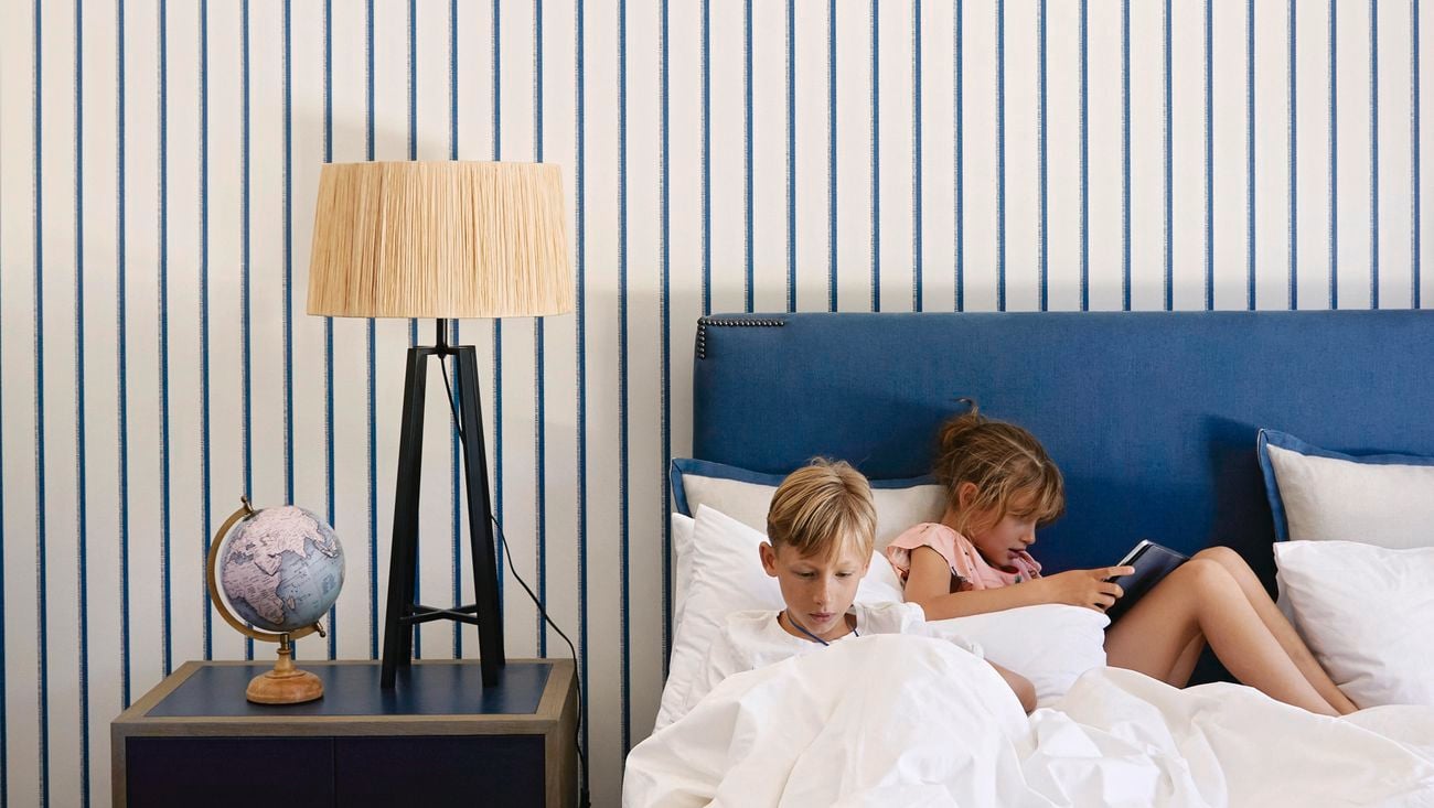 Two kids laying in bed with a white and blue striped wall behind them