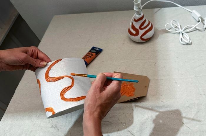 A close-up of a person painting squiggly lines with acrylic paint on a lamp shade