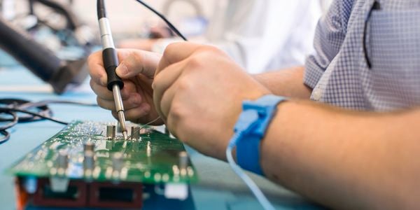 A person using a soldering iron and solder to work on an electronic chip