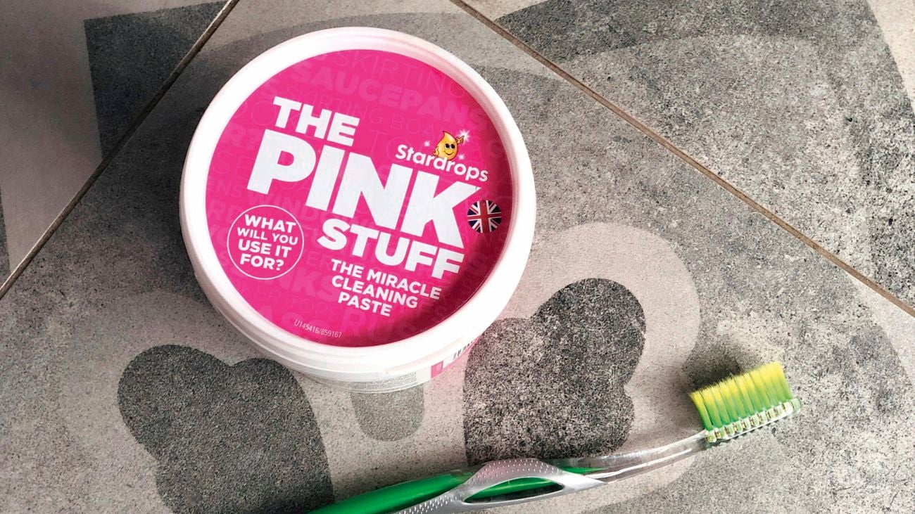 Overhead shot of tub of 'The Pink Stuff' on bathroom tile next to a toothbrush.