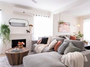 Bright living room with large couch, cushions, throws, white fireplace, mirror, round timber coffee table and sheer curtains