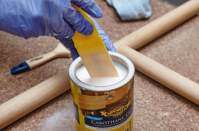 Person dipping brush into tin of varnish.