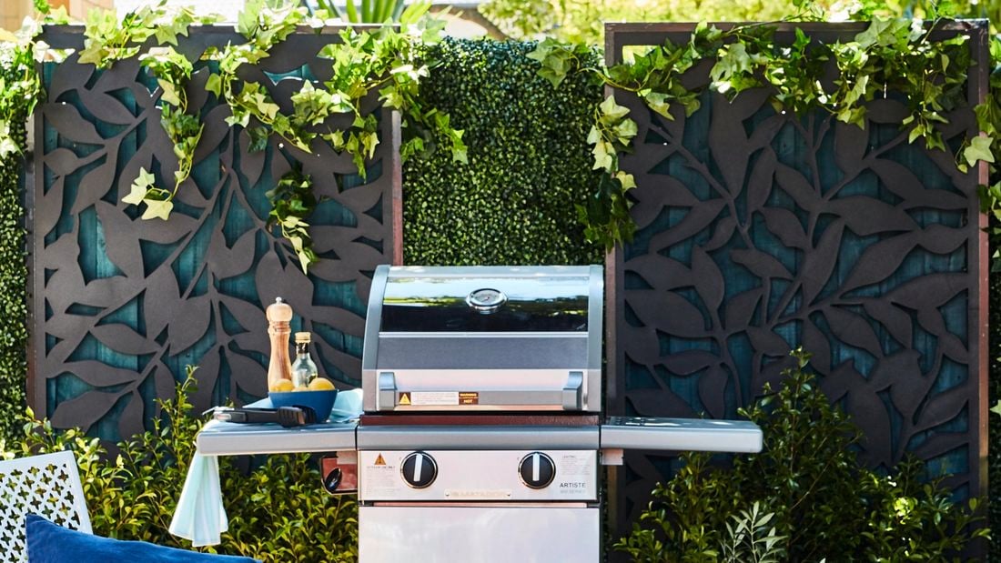 Outdoor entertaining area featuring artificial hedging, privacy screens, BBQ, outdoor furniture and an umbrella.