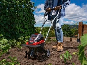 A person using a cordless cultivator machine in the garden.