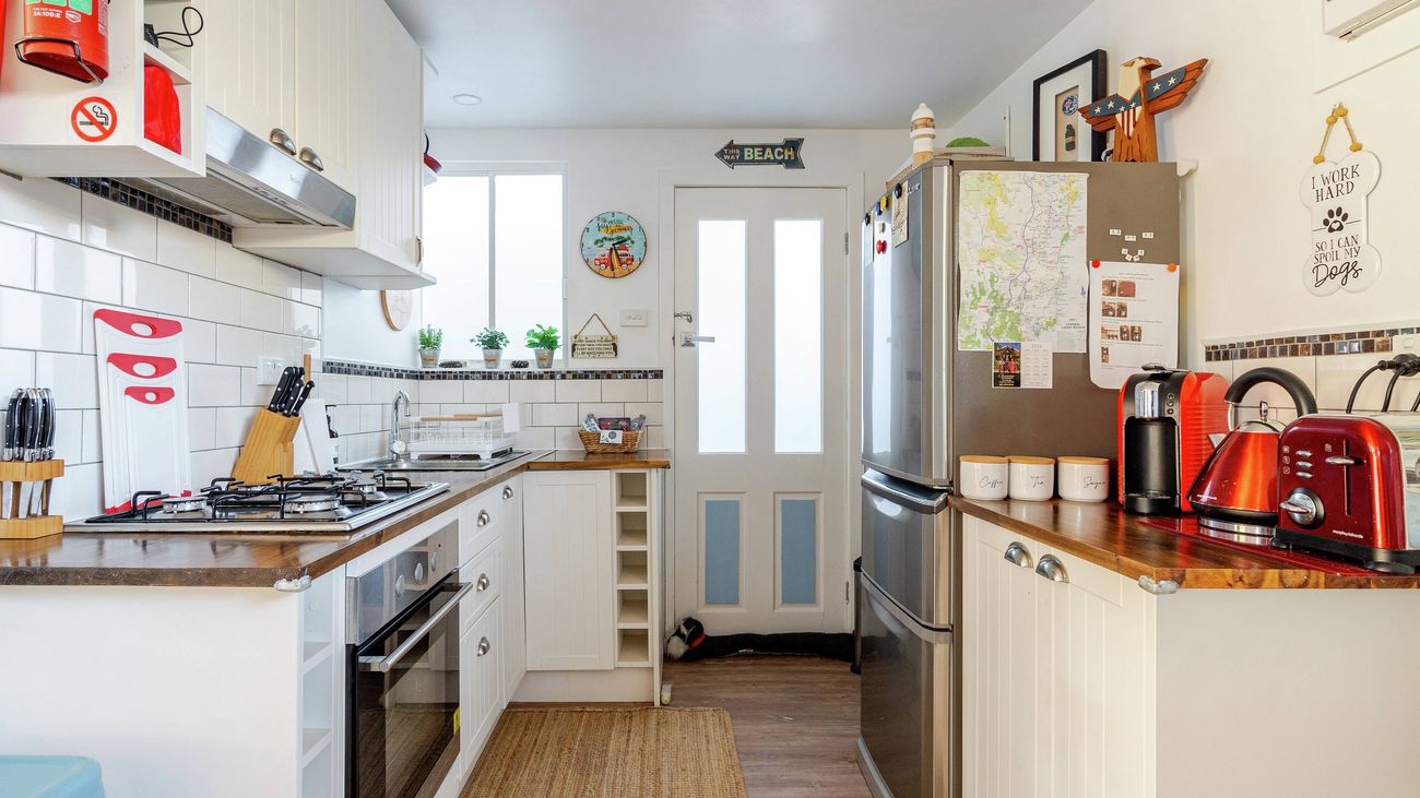 Interior view of a compact kitchen with white cabinetry, wooden benchtops, a stainless steel refrigerator, and appliances.