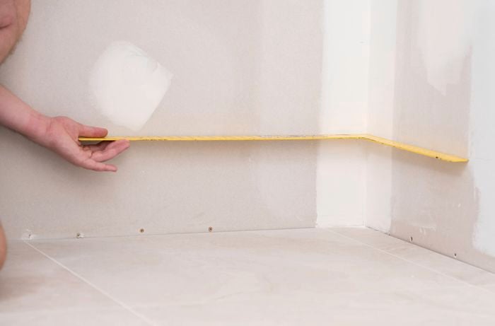A person is using a yellow L-shaped measuring tool to check the corner alignment  of the room is square