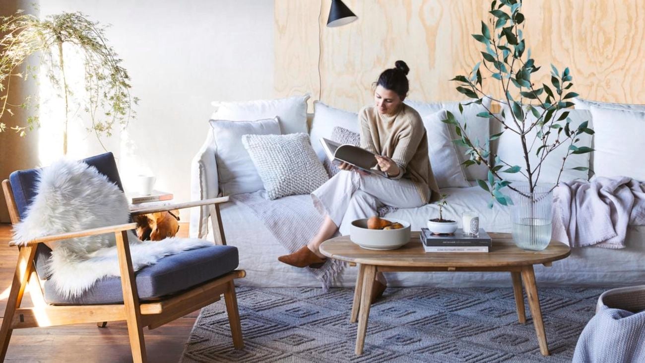 A woman sitting on a grey couch reading a book.