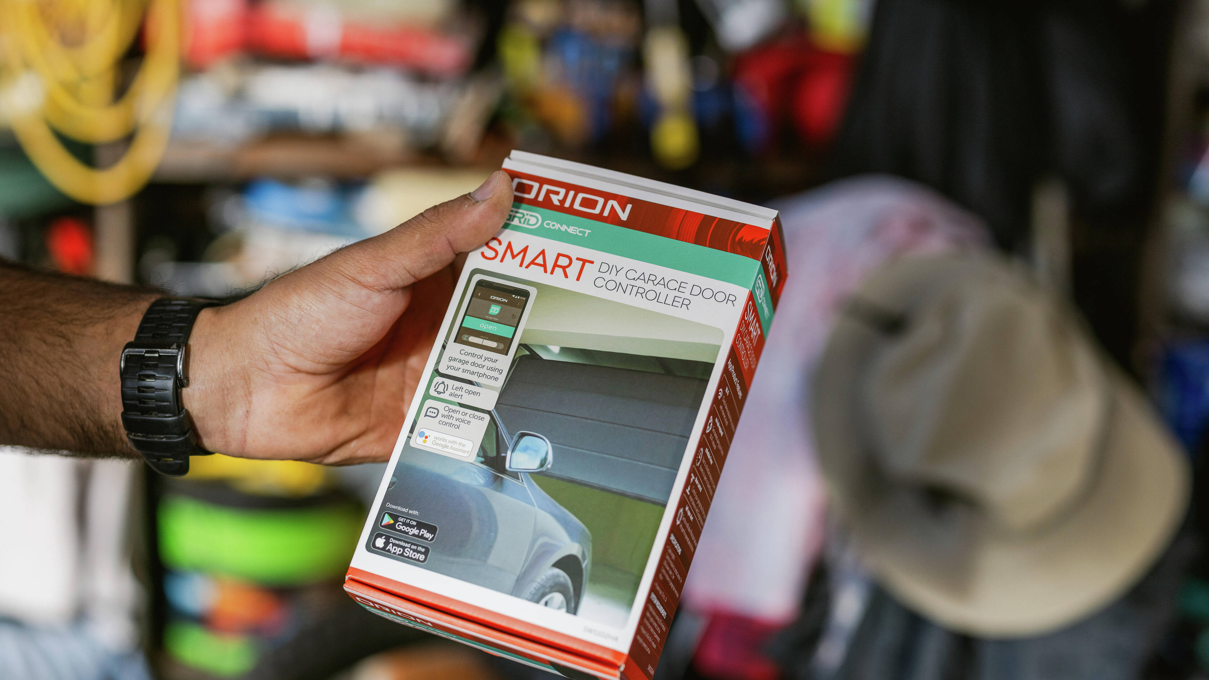 “Hand holding an Orion Grid Connect smart DIY garage door controller box in a workshop setting.”