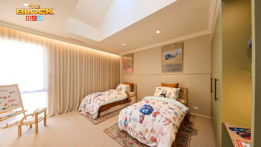 Olive and cream kids bedroom with twin beds and animal print linen, 2 coloured rugs and a kids whiteboard and seat in the corner.