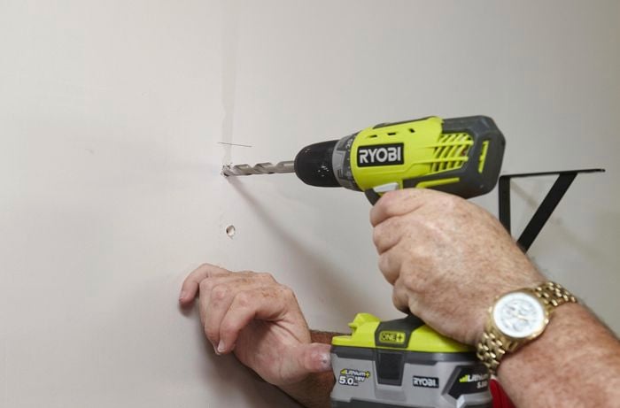 A person drilling a large hole in a plasterboard wall using a cordless drill