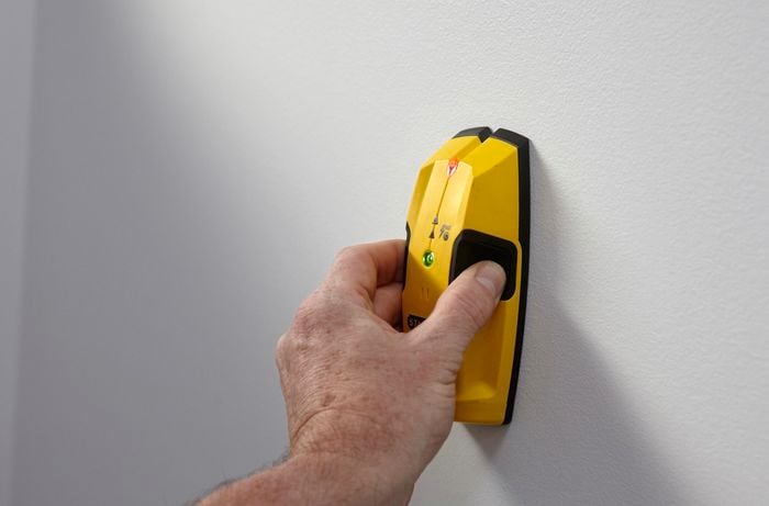 Person holding a stud finder against a wall.