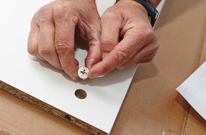 Person inserting cam locks into holes in side panels of cupboard