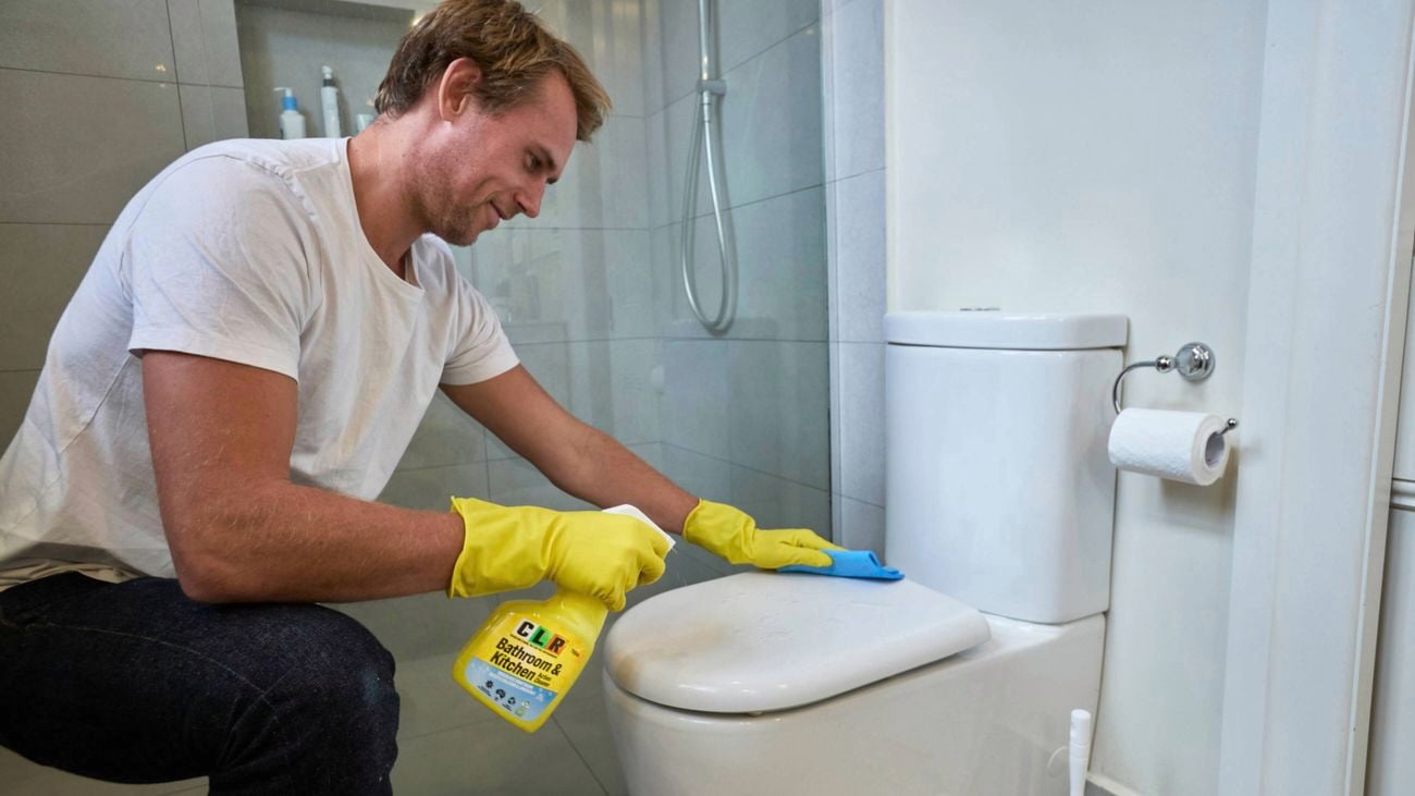 A man in a bathroom cleaning the toilet with CLR Kitchen and Bathroom Cleaner]